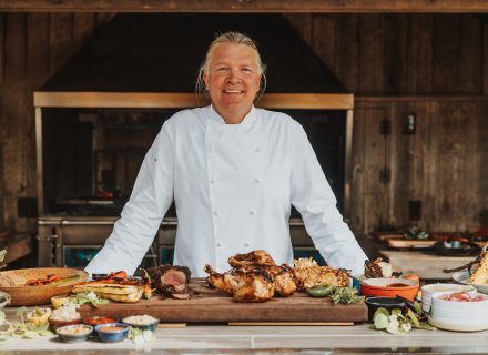 Chef Joshua Drage smiling in his kitchen with a chicken dish sitting ready on his cutting board.
