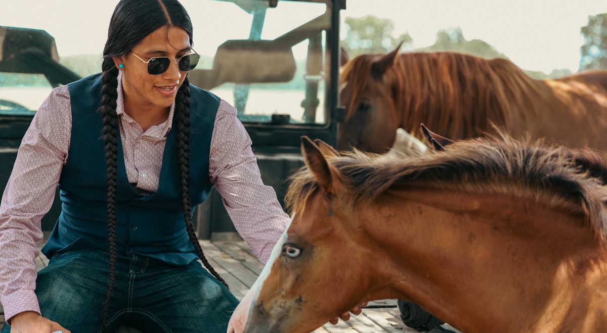 Cole Brings Plenty smiles as he pets horses while sitting on the back of a truck.