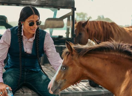 Cole Brings Plenty smiles as he pets horses while sitting on the back of a truck.