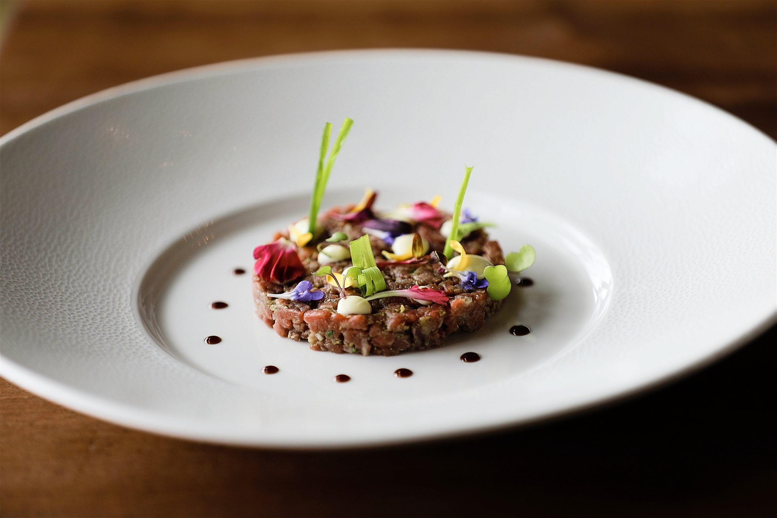 A small wagyu tartare garnished with colorful florals from the Brush Creek Ranch menu sits on a white plate.