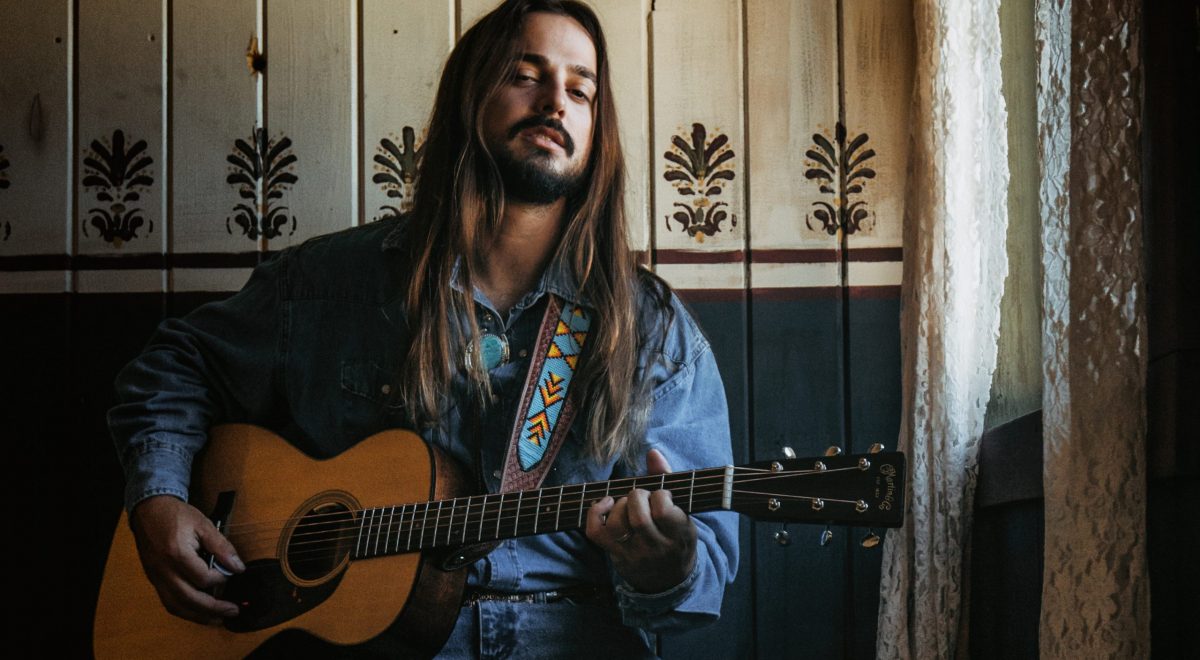 Ian Munsick sits by a window and plays his guitar.