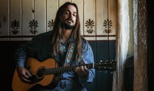 Ian Munsick sits by a window and plays his guitar.