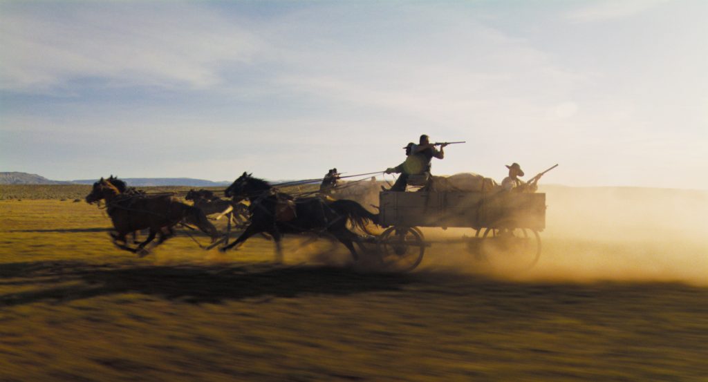 A horse carriage pulling gun-wielding men races across a plain in "Horizon: Part 1."